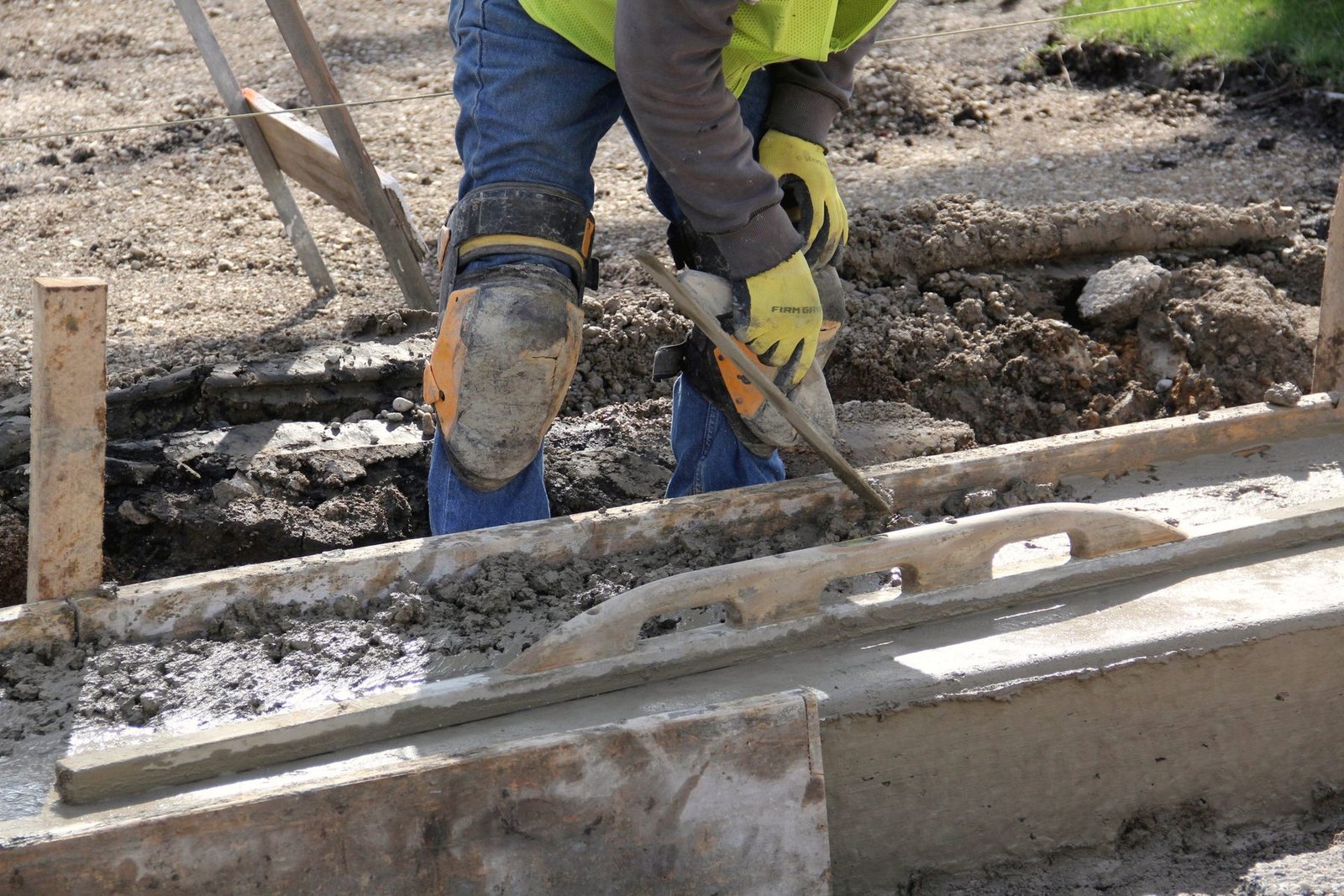 A worker levelling a concrete footing trench with a hand tool.